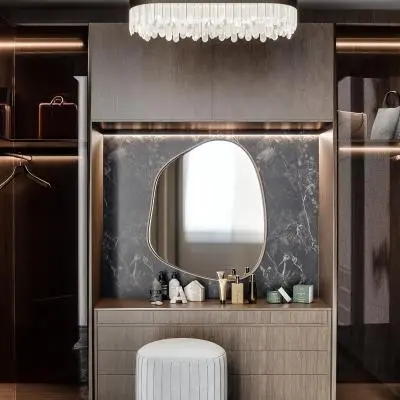 Modern tasarımlı camlı giyinme odası. Ortasında yuvarlak bir puf ve şık bir aydınlatma armatürü ile gösterişli bir görünüm sunan giyinme odası.