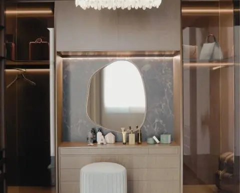 Modern tasarımlı camlı giyinme odası. Ortasında yuvarlak bir puf ve şık bir aydınlatma armatürü ile gösterişli bir görünüm sunan giyinme odası.